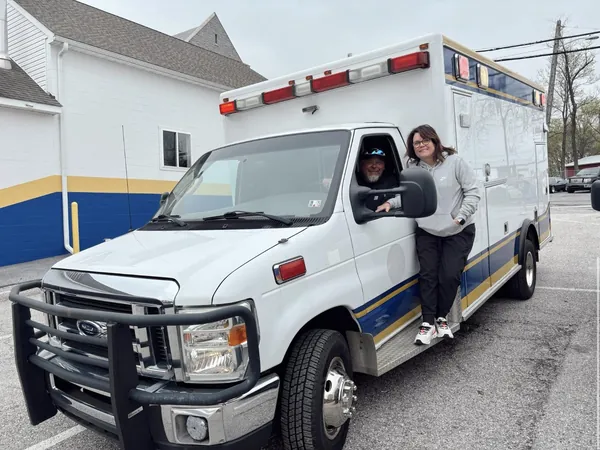 The two owners with the white ambulance they bought, one leaning out of the driver’s window