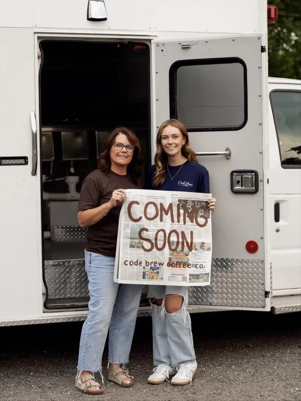 The owners in front of the truck holding a hand-painted Coming Soon, Code Brew Coffee Co. sign