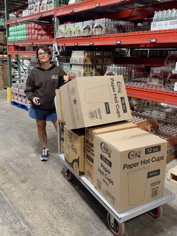 An owner in a Code Brew hoodie at a warehouse store with a cart of paper coffee cups